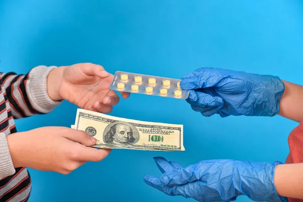 A doctor in blue medical gloves sells packaged pills to a patient for treatment for dollars. Profit and benefit in a corrupt medical environment.