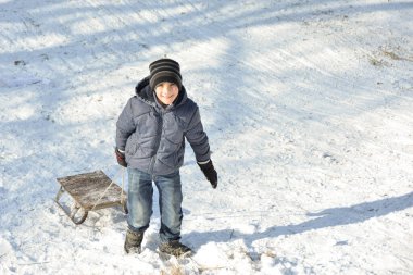 Oğlan kar kaydırağına tırmandı ve kızağı arkasından çekti. Kış kar oyunları.