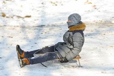 Kızaklı bir çocuk karlı bir tepeden aşağı iniyor. Eğlenceli kış oyunları.