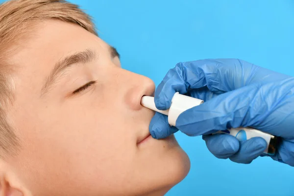 一位戴着蓝色防护手套的耳鼻喉科医生向孩子的鼻子喷洒药物 人类呼吸空洞的治疗 — 图库照片