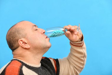 Bir adam mavi kapsüllerle şampanya bardağından ilaç içiyor. Akşamdan kalmalığın ve alkolizmin tedavisi..