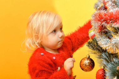 Kırmızı kazaklı küçük bir kız ağacı şenlikli oyuncaklar ve parıltılı süslemelerle süslüyor..