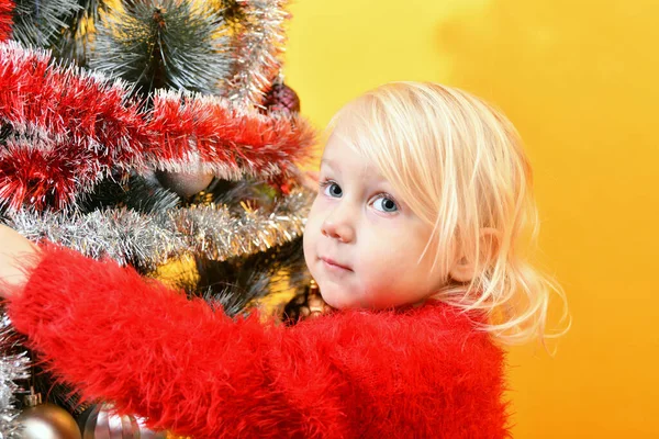赤いセーターの少女がお祝いのおもちゃと輝くティンセルで木を飾ります — ストック写真