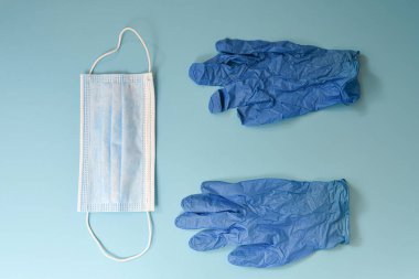 Mavi eldivenler ve açık mavi bir arka planda koruyucu bir maske..