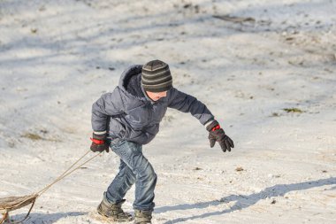 Kızaklı bir çocuk karlı bir tepeye tırmanıyor..