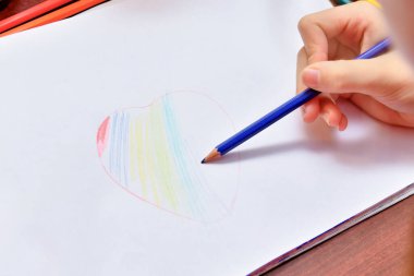 Kız beyaz bir kağıda renkli kalemlerle bir kalp çiziyor..