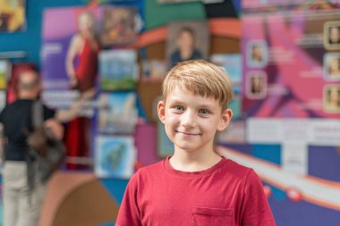 Sanat galerisinde neşeli bir çocuk gülümser ve sergi salonundaki resimlerin arka planına karşı poz verir..