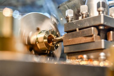 Dönüştürücü, torna tezgahında bronz bir parçadaki deliği elektrikli bir aletle sıkar..