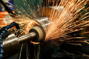 Kıvılcımları olan silindirik bir öğütücüde aşındırıcı bir tekerlekle hırpalanmak.