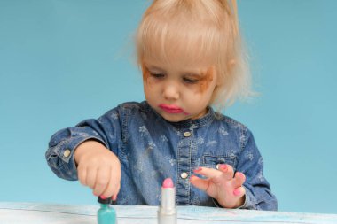 Küçük çocuk ojeyle oje sürüyor. Çocuklar yetişkin gibi görünmek için ebeveyn kozmetik ürünleri kullanırlar..