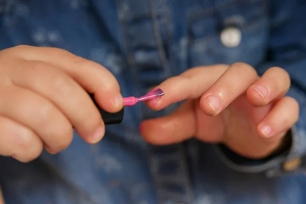 stock image A little girl ineptly paints her nails with varnish from her mother's cosmetics.