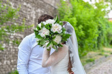 Gelin kendini bir buket çiçekle kapladı ve damadı öptü. Gelinin elinde bir buket şakayık.