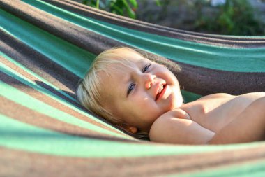 Küçük bir kız hamakta yatıyor ve akşam güneşinden gözlerini kısıyor..