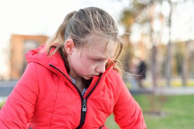 Kırmızı ceketli bir kız rahatsız oldu ve parkta otururken ağlıyor..