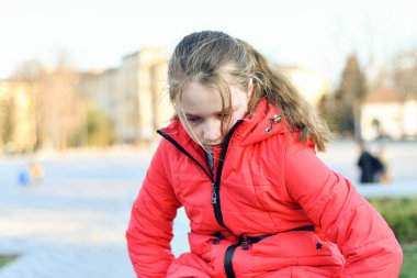 Kırmızı ceketli bir kız rahatsız oldu ve parkta otururken ağlıyor..