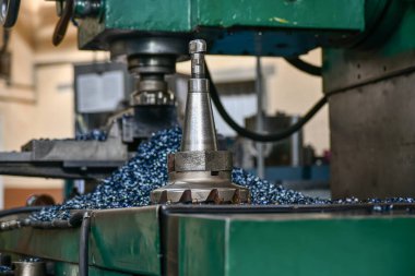 Metal işleme sonrası çiplerin arka planına karşı bir değirmen makinesinin çerçevesindeki yüz değirmenleme kesicisi.