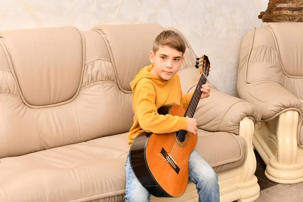 男の子は革のソファに座ってギターを弾いている — ストック写真