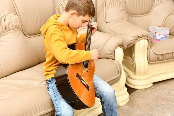 Menino Está Sentado Sofá Couro Tocando Guitarra — Fotografia de Stock