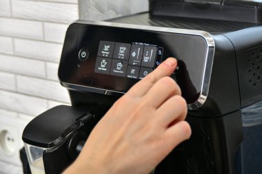 Bir kadın kahve makinesinde espresso ya da kapuçino yapmak için mod seçer..