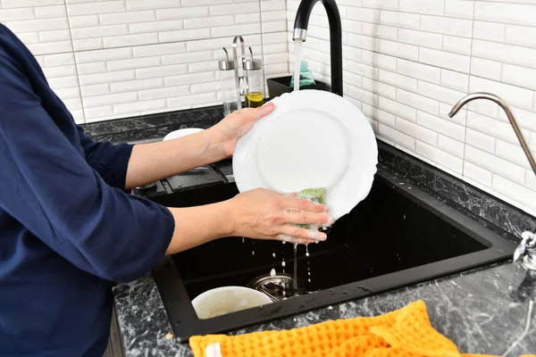 A woman washes dishes in the kitchen with tap water.