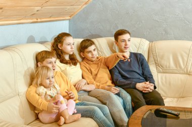 Beş çocuk televizyon izliyor ve uzaktan kumandayla kanal değiştiriyor..