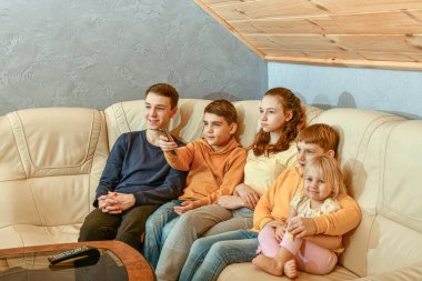 Dost canlısı çocuklar akşamları deri koltukta otururken televizyon izler..