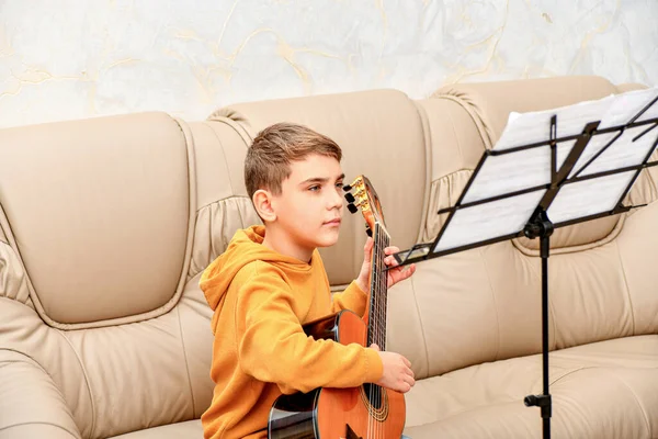 Adolescente Aprende Tocar Guitarra Mira Las Notas Arrancando Las Cuerdas Imagen de stock