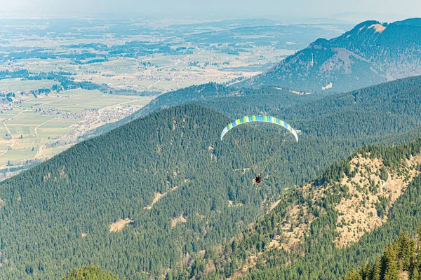 Man paragliding in the air between high mountains.