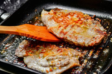 Kızarmış domuz bifteği kızartma tavasında. Bir kadın eti kızartmaya çevirir..