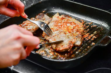 Bir kadın tavada çatal ve bıçakla kızarmış domuz bifteği keser..