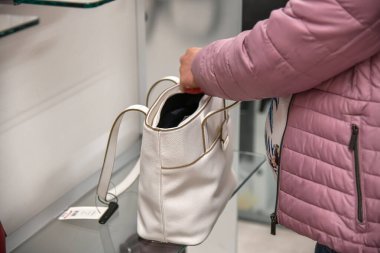 Bir kız alışveriş merkezinde beyaz deri bir çanta seçer ve ölçer..