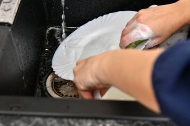 Bir kadın mutfakta musluk suyuyla bulaşık yıkıyor..