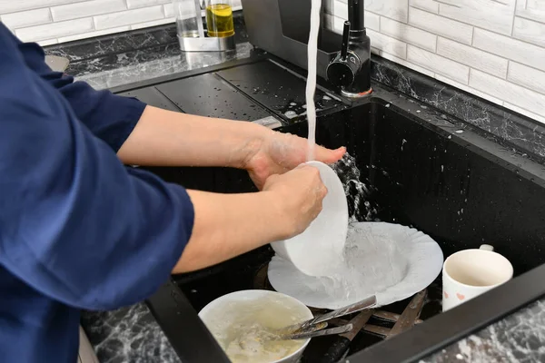 A woman washes dishes in the kitchen with tap water.