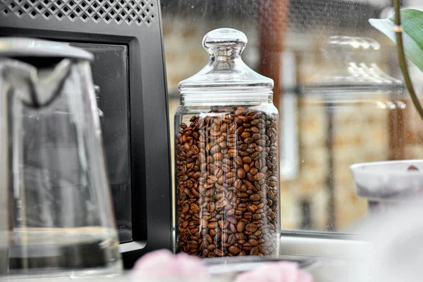 Roasted coffee beans in a glass container next to the coffee machine in the kitchen.