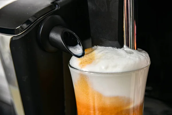 Coffee with foam and milk in a glass cup, prepared in a coffee machine.
