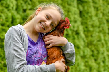 Neşeli bir kız elinde bir tavuk tutuyor ve ona sarılıyor..