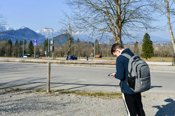 A young man with a backpack got lost and is looking for a way using a map on his phone. The concept of traveling alone.