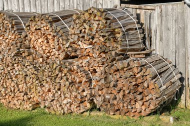 Sawn firewood for residential heating is stacked near the fence.