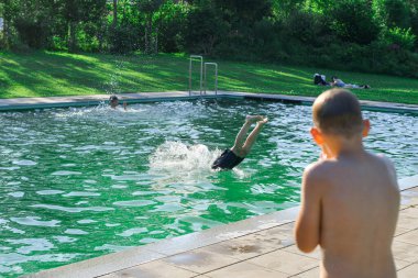 A boy in the pool watches his friend jump into the water.