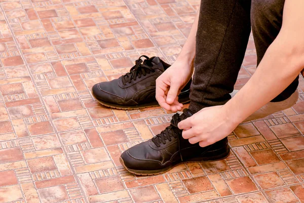 A man puts on sneakers and ties his shoelaces at home in the hallway.