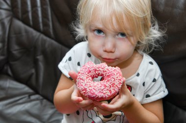 Küçük bir kız kremalı lezzetli bir kırmızı çörek yiyor..