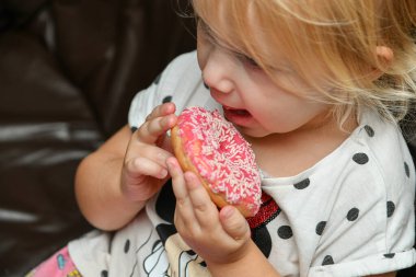 Küçük bir kız kremalı lezzetli bir kırmızı çörek yiyor..