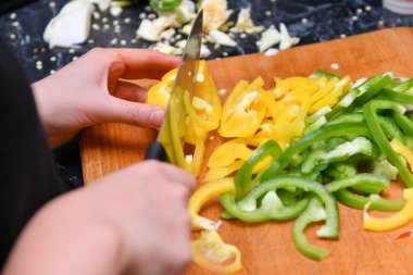 Küçük parçalara ayrılmış sarı ve yeşil biberler mutfaktaki kesme tahtasının üzerinde yatıyor..