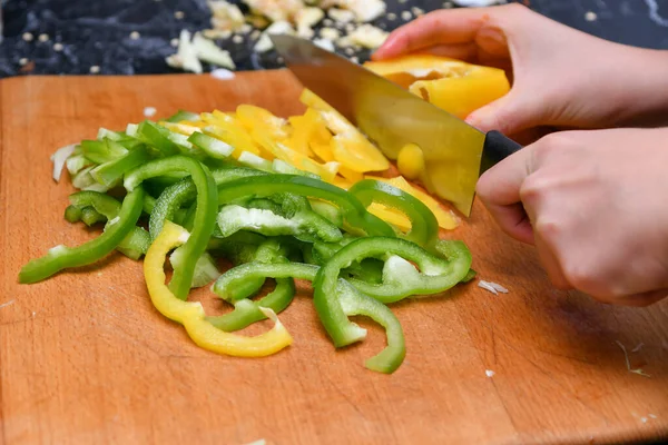 Mutfakta bir kadın sarı ve yeşil biberleri küçük parçalara ayırıyor..
