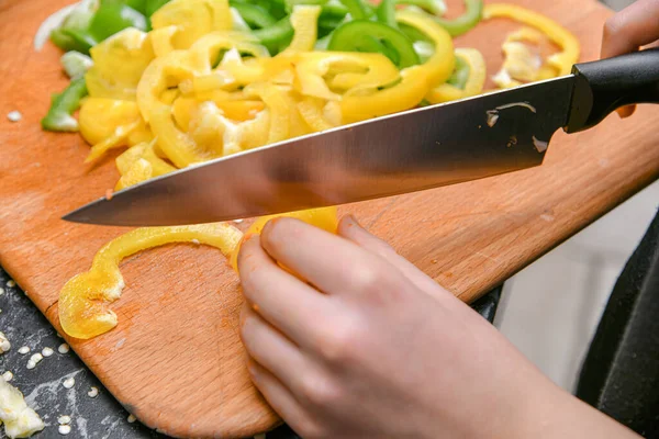 Mutfakta bir kadın sarı ve yeşil biberleri küçük parçalara ayırıyor..