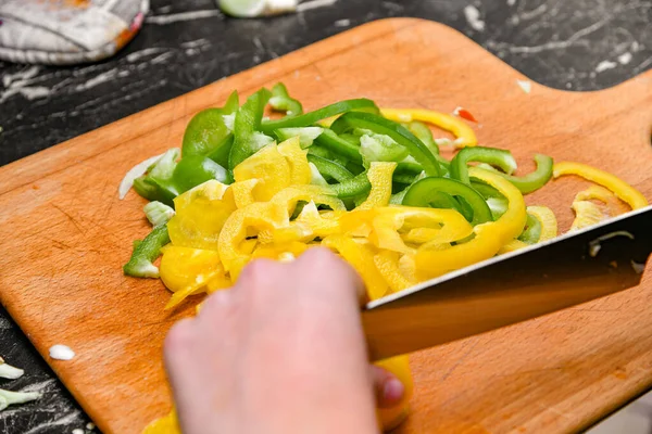 A woman in the kitchen cuts yellow and green peppers into small pieces.