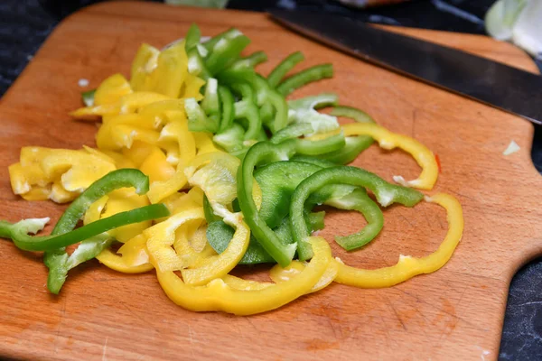 Yellow and green peppers cut into small pieces lie on a cutting board in the kitchen.