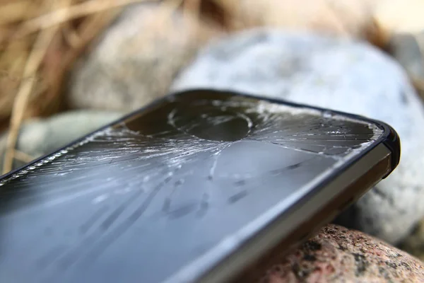 Mobile phone with broken display lying on rocks.