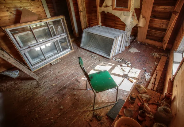 Ruined interior of an old wooden house with chair and disused windows.