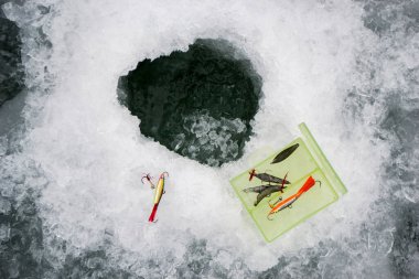 Küçük bir balıkçı, buz deliğinin yanında balık tutmak için yem ve teçhizat dolu bir kumbara kutusu. Balık yemi ve aksesuarlar. Balık yemi takımı..